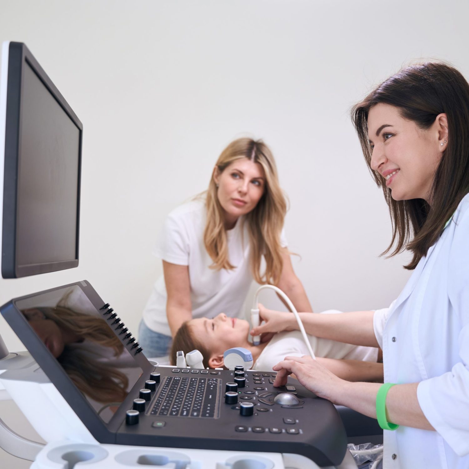 Child with his mother in ultrasound room for ultrasound of the thyroid gland, doctor looks at monitor of the apparatus